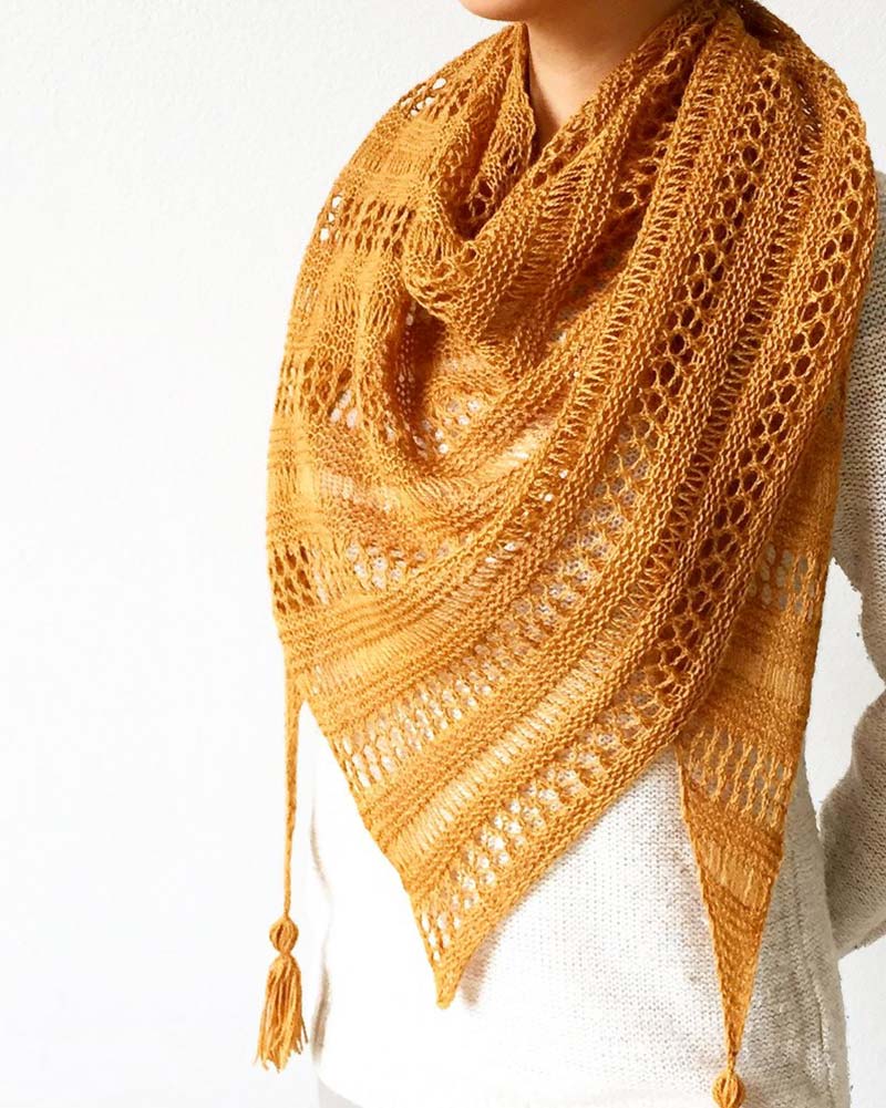 This shawl offers the perfect blend of elegance and coziness with its asymmetrical design, knitted from the corner to form a triangle with tassels on the corners.